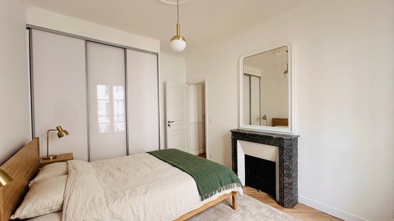 La chambre meublée : lit de chêne et linge de lin dans l'axe de la cheminée de marbre, lampes de laiton.