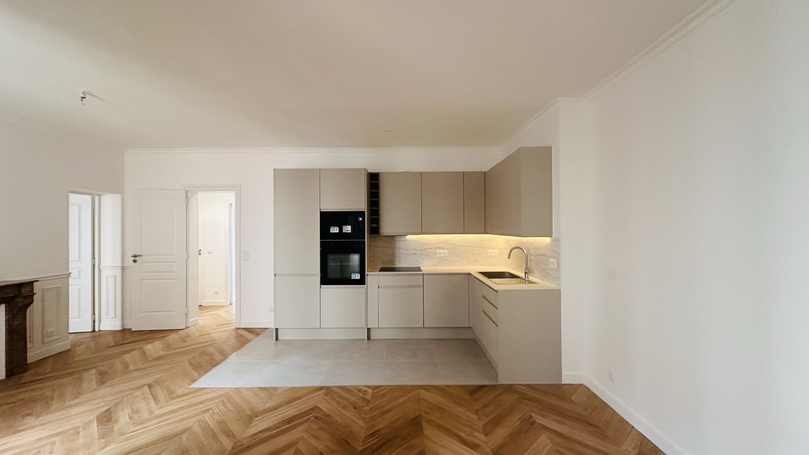 La cuisine ouverte taupe : façades lisses, plan veiné, bandeau lumineux sous les meubles hauts.