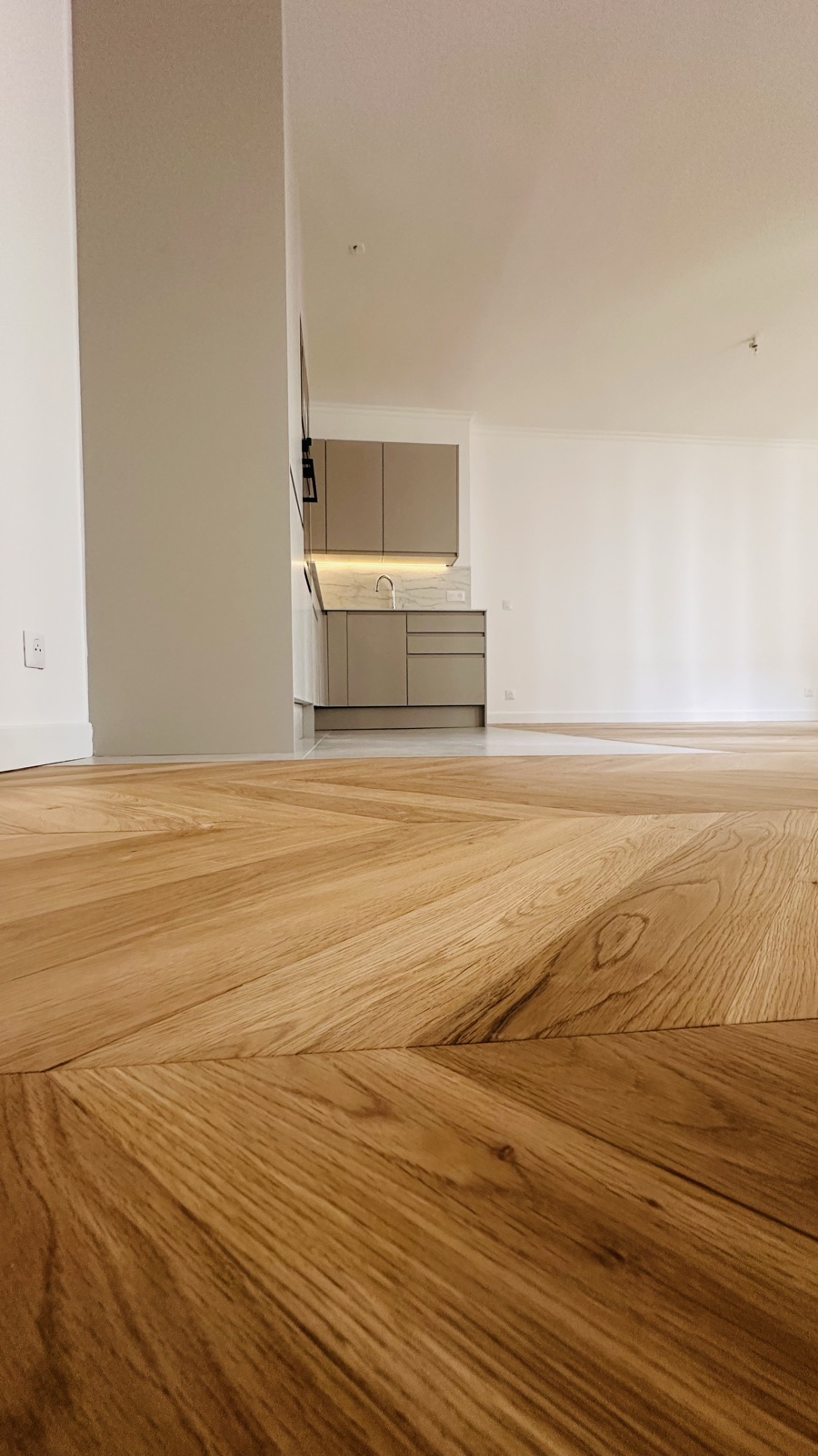 Le parquet Point de Hongrie au ras du sol, chevrons de chêne filant vers la cuisine.