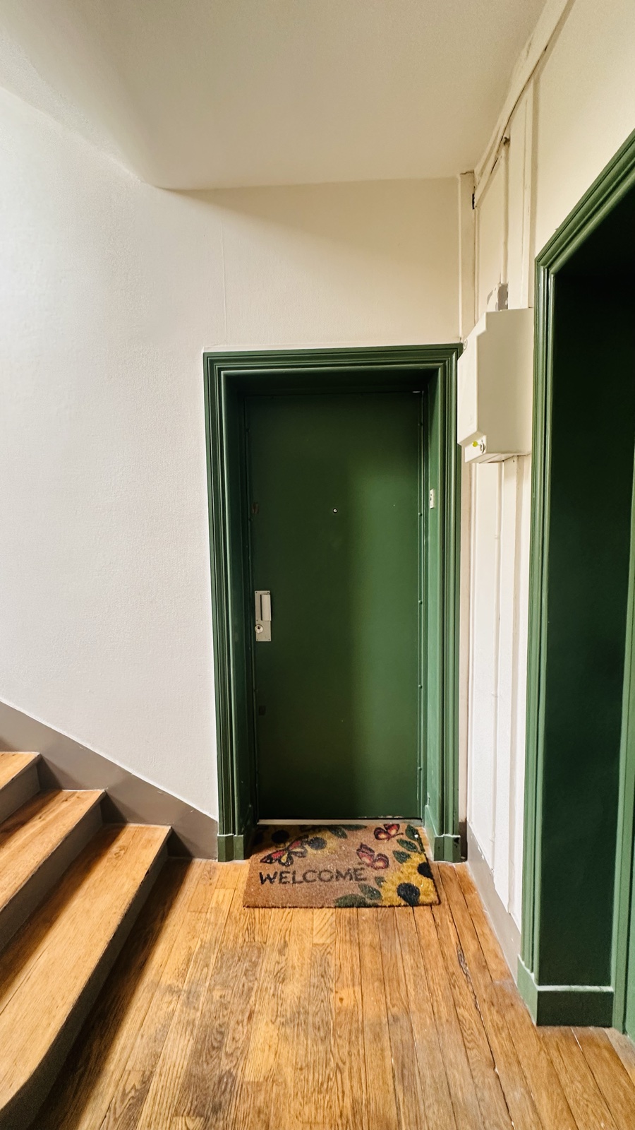La porte palière repeinte en vert profond, parquet ancien du palier.