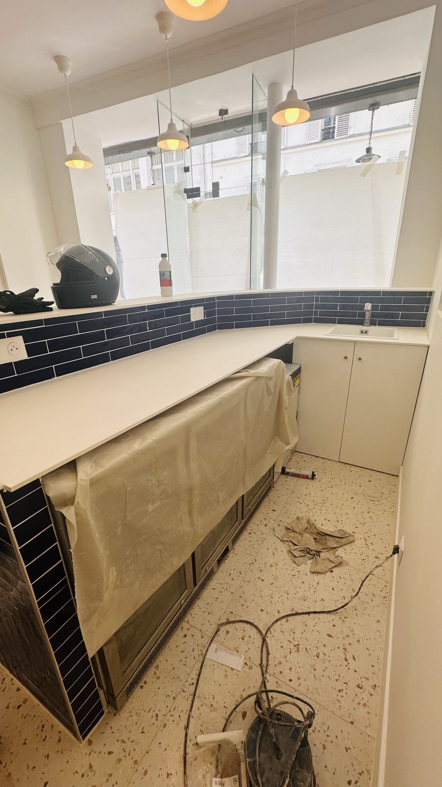 Le comptoir en cours de chantier, plan protégé, faïence bleu nuit déjà posée au mur, sol terrazzo bâché.