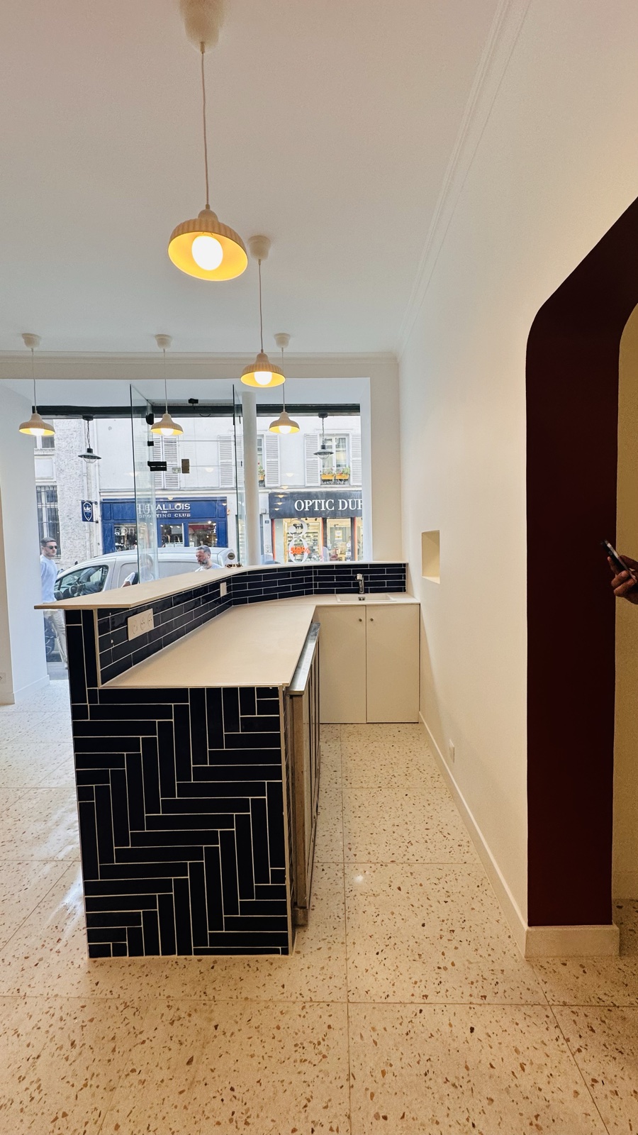 Le comptoir fini, zellige bleu nuit posé en chevrons, arche bordeaux en fond, sol terrazzo.