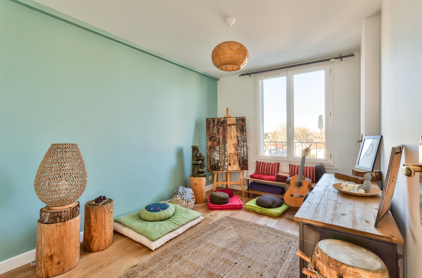 Pièce de musique aux murs vert d'eau : guitare, coussins de sol, tapis de jute et suspension en fibres tressées.